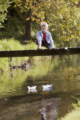 Junge (10-12) auf Brücke beobachtet Papierboote im Wasser - RDF00171