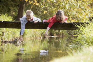 Junge (10-13) und Mädchen (7-9) liegen auf einer Brücke und beobachten Papierboote im Wasser - RDF00170