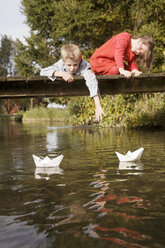 Boy (10-12) and girl (7-9) on bridge watching paper boats in water - RDF00169