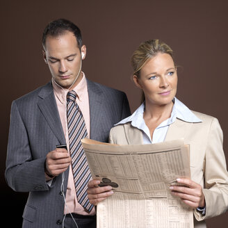 Businessman and businesswoman, man listening to mp3 player, woman holding newspaper - JLF00249
