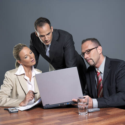 Geschäftsleute mit Blick auf Laptop am Konferenztisch, lizenzfreies Stockfoto