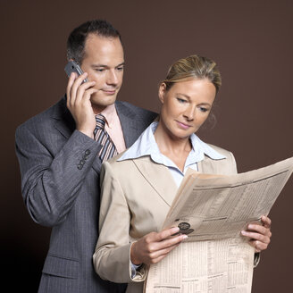 Businessman and businesswoman man using mobile phone, woman holding newspaper - JLF00221