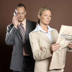 Businessman and businesswoman man using mobile phone, woman holding newspaper - JLF00219