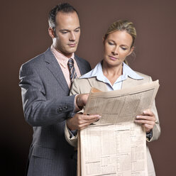 Businessman and businesswoman man holding newspaper - JLF00206