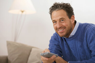 Man sitting on sofa, holding remote control - WESTF03386
