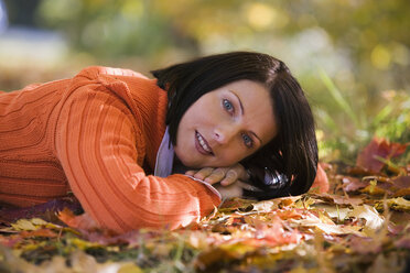 Woman lying on autumn leaves, close-up, portrait - WESTF03112