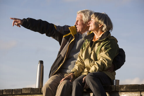 Senior couple sitting on jetty, man pointing - WESTF03514