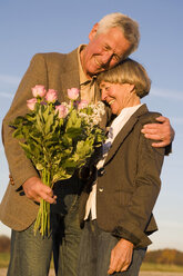 Senior couple embracing, man holding bouquet - WESTF03482