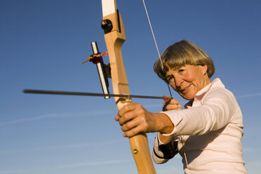 Senior adult woman using bow and arrow - WESTF03465