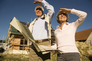 Älteres Ehepaar mit Plan vor einem teilweise gebauten Haus - WESTF03455