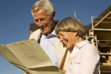 Älteres Ehepaar mit Plan vor einem teilweise gebauten Haus - WESTF03453