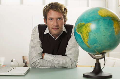 Junger Mann sitzt am Schreibtisch, Globus im Vordergrund - WESTF03541