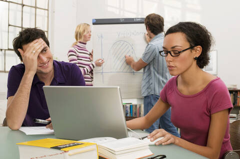 Junges Paar steht am Flipchart, Fokus auf Mann und Frau, die im Vordergrund einen Laptop benutzen, lizenzfreies Stockfoto