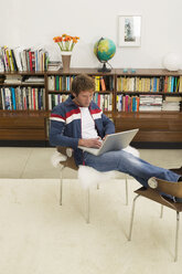 Junger Mann sitzt auf einem Stuhl und benutzt einen Laptop - WESTF03608