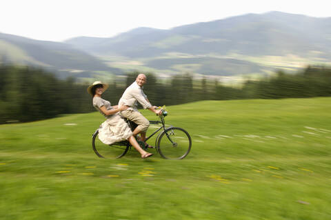 Paar fährt Fahrrad auf einer Wiese, Seitenansicht, lizenzfreies Stockfoto