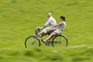 Paar fährt Fahrrad auf einer Wiese, Seitenansicht - HHF00900