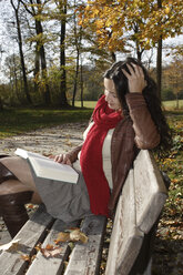 Young woman sitting on bench, reading book - LDF00411