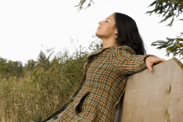 Junge Frau sitzt auf einer Bank, Augen geschlossen - LDF00370