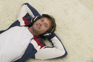 Young man lying on floor, wearing headphones, elevated view - WESTF03683