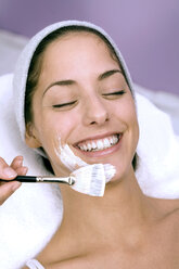 Young woman having face mask applied with make-up brush, smiling, close-up - WESTF03141