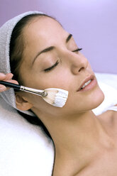 Young woman having face mask applied with make-up brush, eyes closed, close-up - WESTF03139