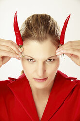 Young woman holding chili on head, simulating horns, portrait - LDF00435