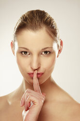 Young woman holding forefinger on lips, smiling, portrait - LDF00416
