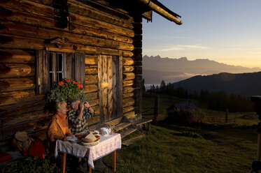 Älteres Paar sitzt vor einer Berghütte und beobachtet den Sonnenuntergang - HHF01134