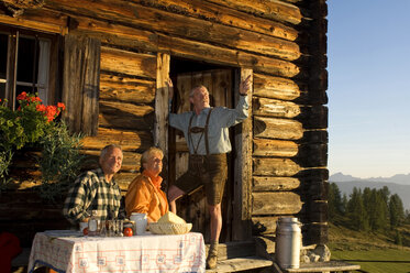 Älteres Paar sitzt vor einer Almhütte und spricht mit einem Bauern - HHF01130