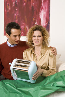 Couple sitting on sofa, woman holding toaster - WESTF03979