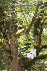 Junge Frau meditiert auf einem Baumzweig, Seitenansicht - HHF01149