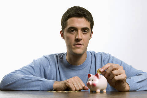 Young man plugging coin in piggy bank, lizenzfreies Stockfoto
