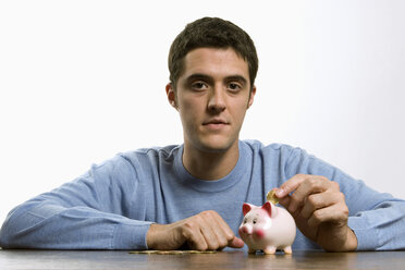 Young man plugging coin in piggy bank - LDF00471