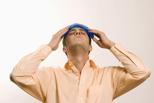 Young man holding ice pack on head, eyes closed - LDF00459