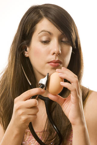 Junge Frau hält Stethoskop auf Ei, lizenzfreies Stockfoto