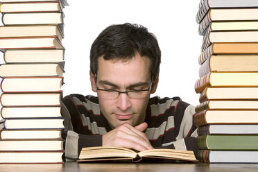 Junger Mann liest neben gestapelten Büchern - CLF00305