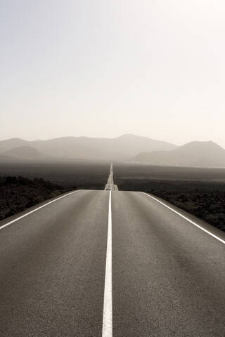 Spanien, Lanzarote, leere Straße durch Landschaft, lizenzfreies Stockfoto