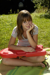 Teenager-Mädchen (16-17) sitzt auf einer Wiese und hält einen Wagen - WESTF04430