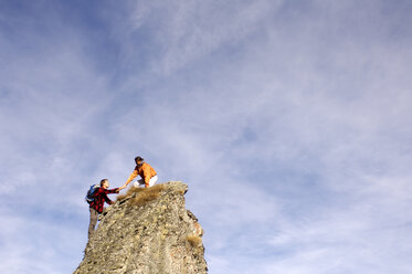 Young couple climbing on mountain peak, woman helping man, side view - WESTF04274