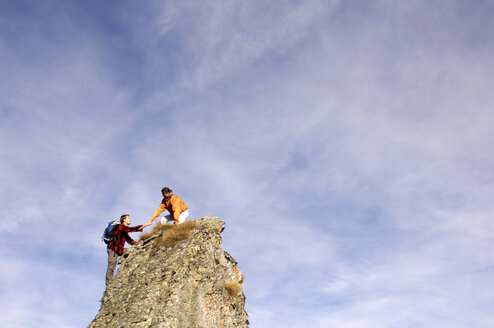 Junges Paar klettert auf Berggipfel, Frau hilft Mann, Seitenansicht - WESTF04274