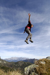 Man jumping over mountains, arms out, side view - WESTF04267