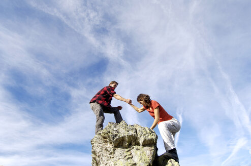 Young couple climbing on mountain peak, man helping woman, low angle view - WESTF04220