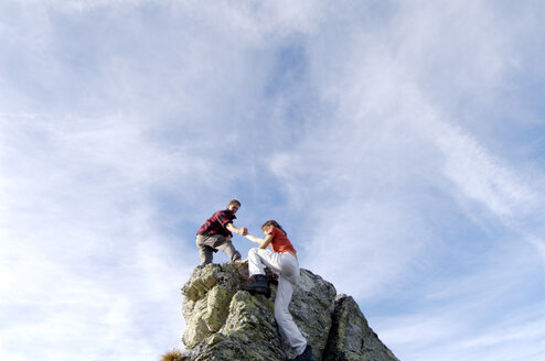 Young couple climbing on mountain peak, man helping woman, low angle view - WESTF04218