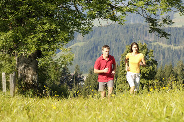 Junges Paar joggt auf einer Wiese, Berge im Hintergrund - WESTF04205