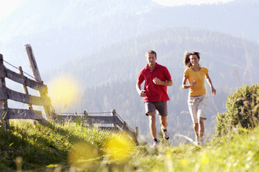 Deutschland, Bayern, junges Paar joggt am Holzzaun, Berge im Hintergrund - WESTF04201