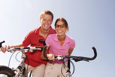 Young couple on bicycle, smiling, low angle view, portrait - WESTF04169