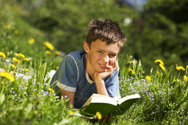 Boy in field reading book, resting head on hand - WWF00277