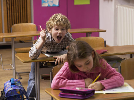 Junge (4-7) schreit hinter Mädchen im Klassenzimmer - WESTF04596