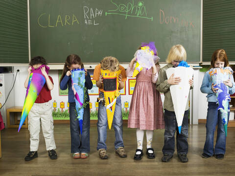 Children (4-7) standing in front of blackboard looking in to school cones stock photo