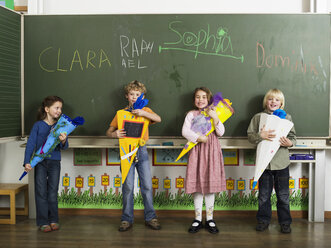 Children (4-7) standing in front of blackboard holding school cones - WESTF04592